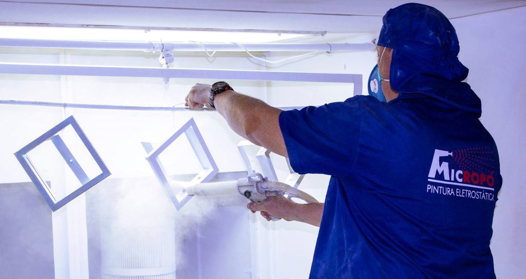 Fotografia retangular de um homem branco com uniforme azul trabalhando com um aplicador de tinta.